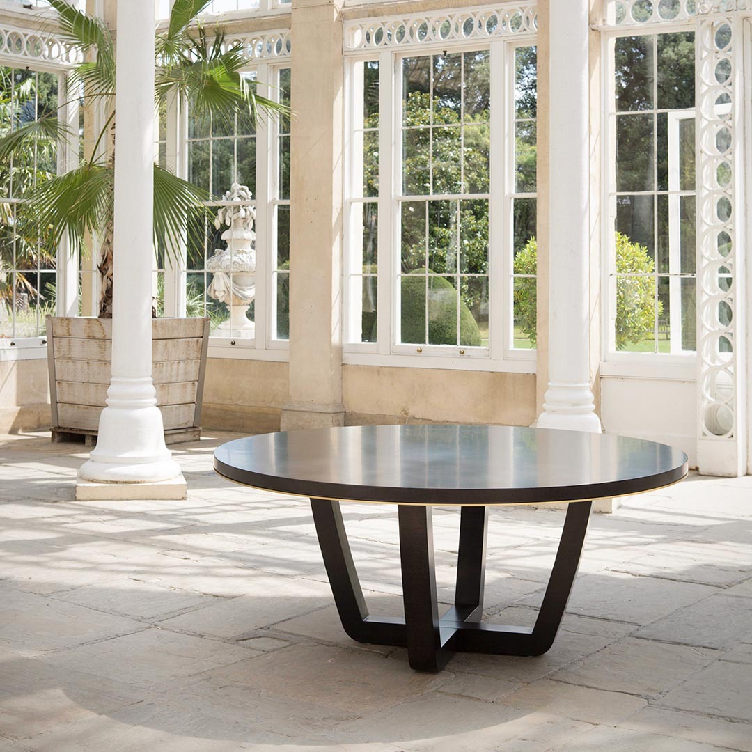 An elegant and contemporary round table combining soft, graceful curves and clean angles for an effortlessly stylish dining room addition. This dark-tinted oak table offers a smooth, modern finish suitable for daily dining with a smart antiqued brushed brass trim to the table edge.
