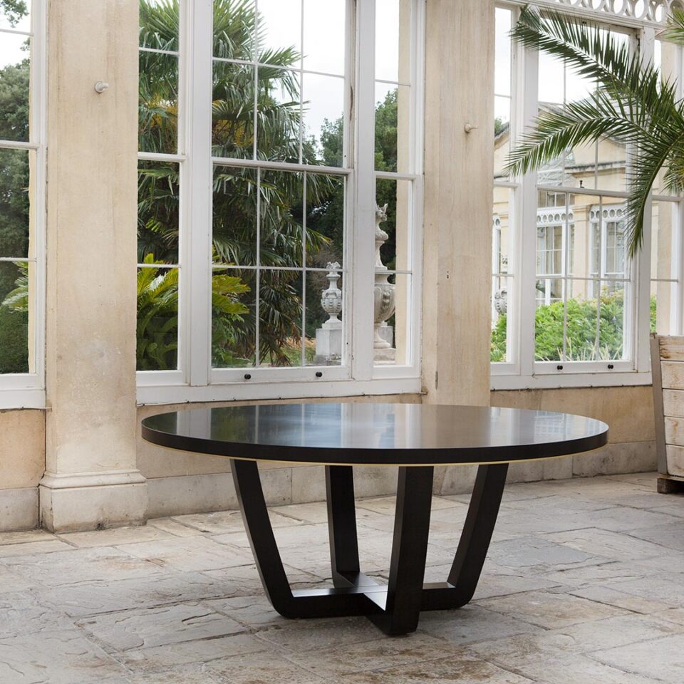 An elegant and contemporary round table combining soft, graceful curves and clean angles for an effortlessly stylish dining room addition. This dark-tinted oak table offers a smooth, modern finish suitable for daily dining with a smart antiqued brushed brass trim to the table edge.