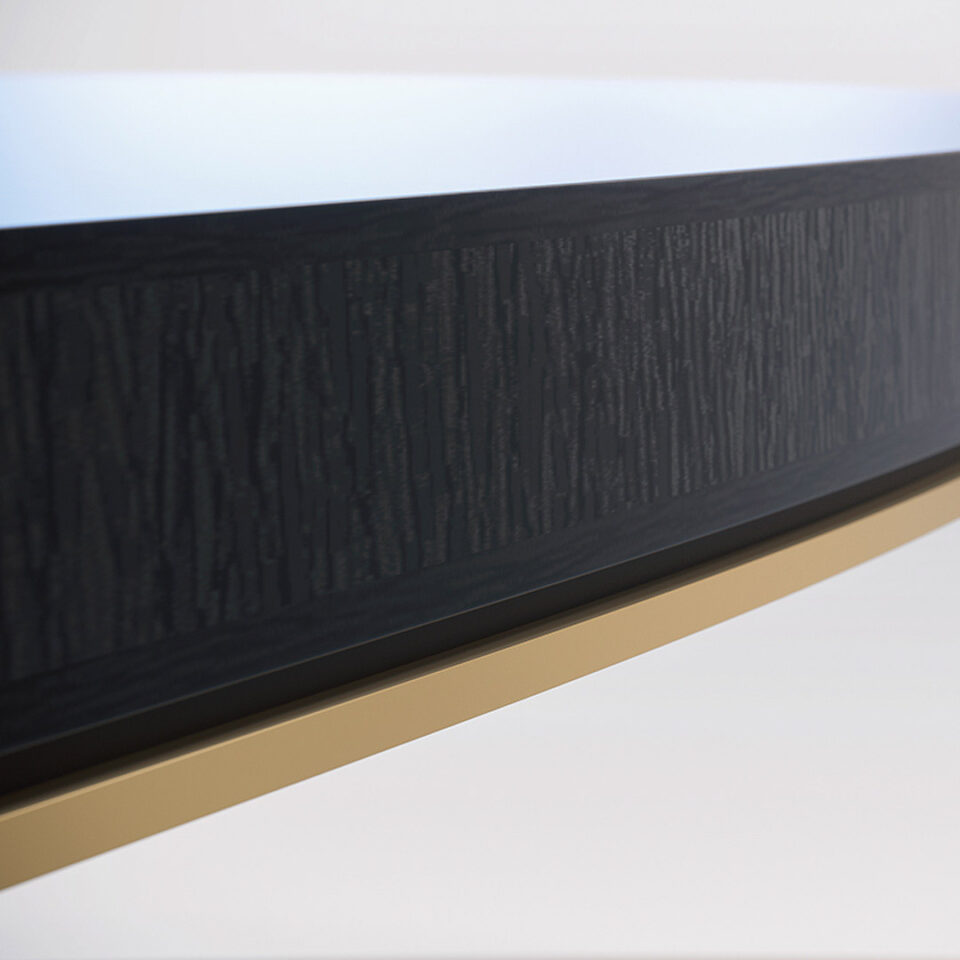 A contemporary dining table in a sycamore black with a shadow gap and brushed brass trim detail to the frieze.