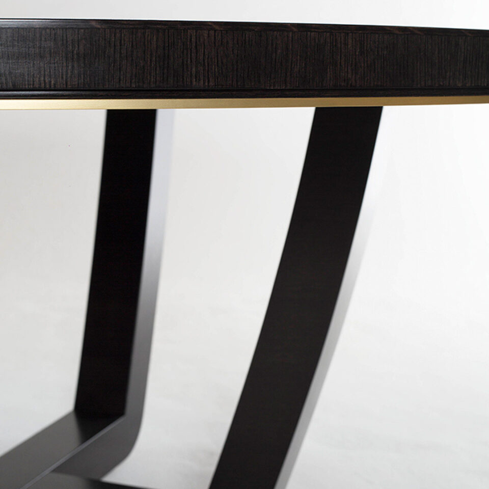 A contemporary dining table in a sycamore black with a shadow gap and brushed brass trim detail to the frieze.