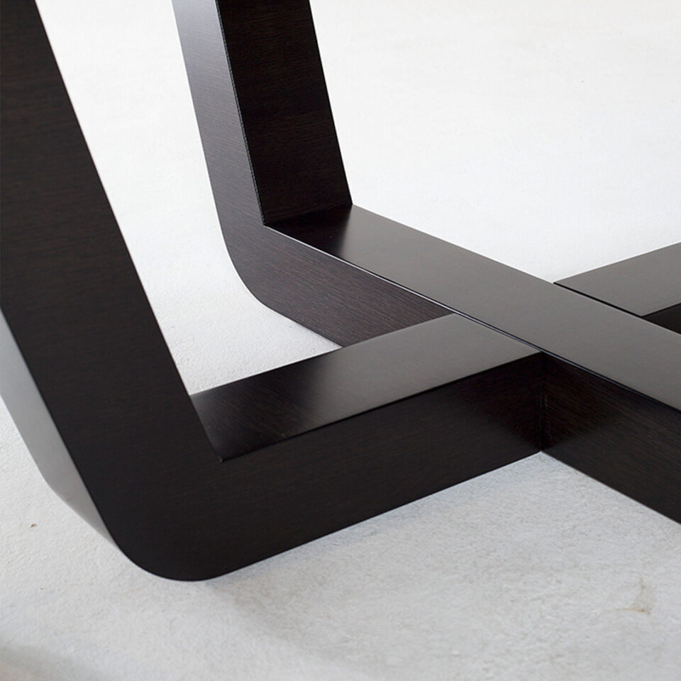 A contemporary dining table in sycamore black with a with cruciform sled legs designed with tempered angles for a gentle, modern look.