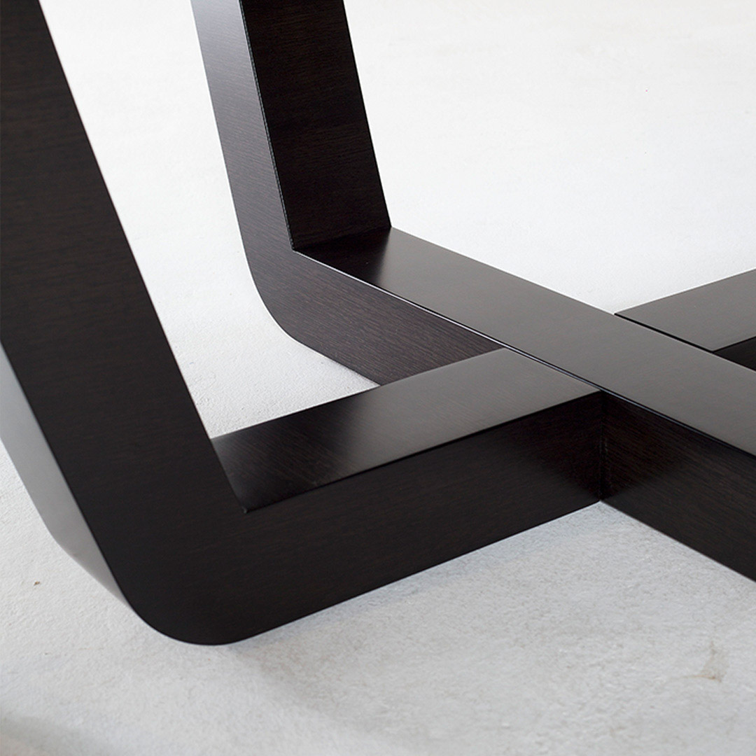 A contemporary dining table in sycamore black with a with cruciform sled legs designed with tempered angles for a gentle, modern look.