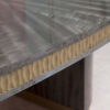 A detail frieze image of this glamorous dining table finished in a pebble grey anegre with a hand carved liquid bronze relief trim