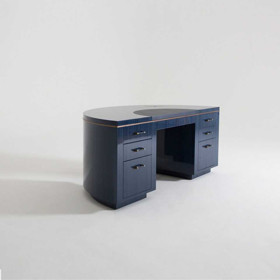 A deluxe writing desk in a figured blue eucalyptus timber in a high gloss finish with antiqued brushed brass detailing and a blue leather writing surface. Side view. Design by DAVIDSON London.