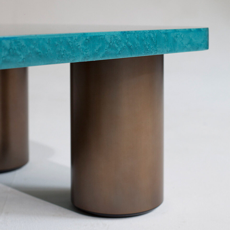 A glamorous coffee table finished in a stylish blue birdseye maple with four cylindrical antique brushed brass legs