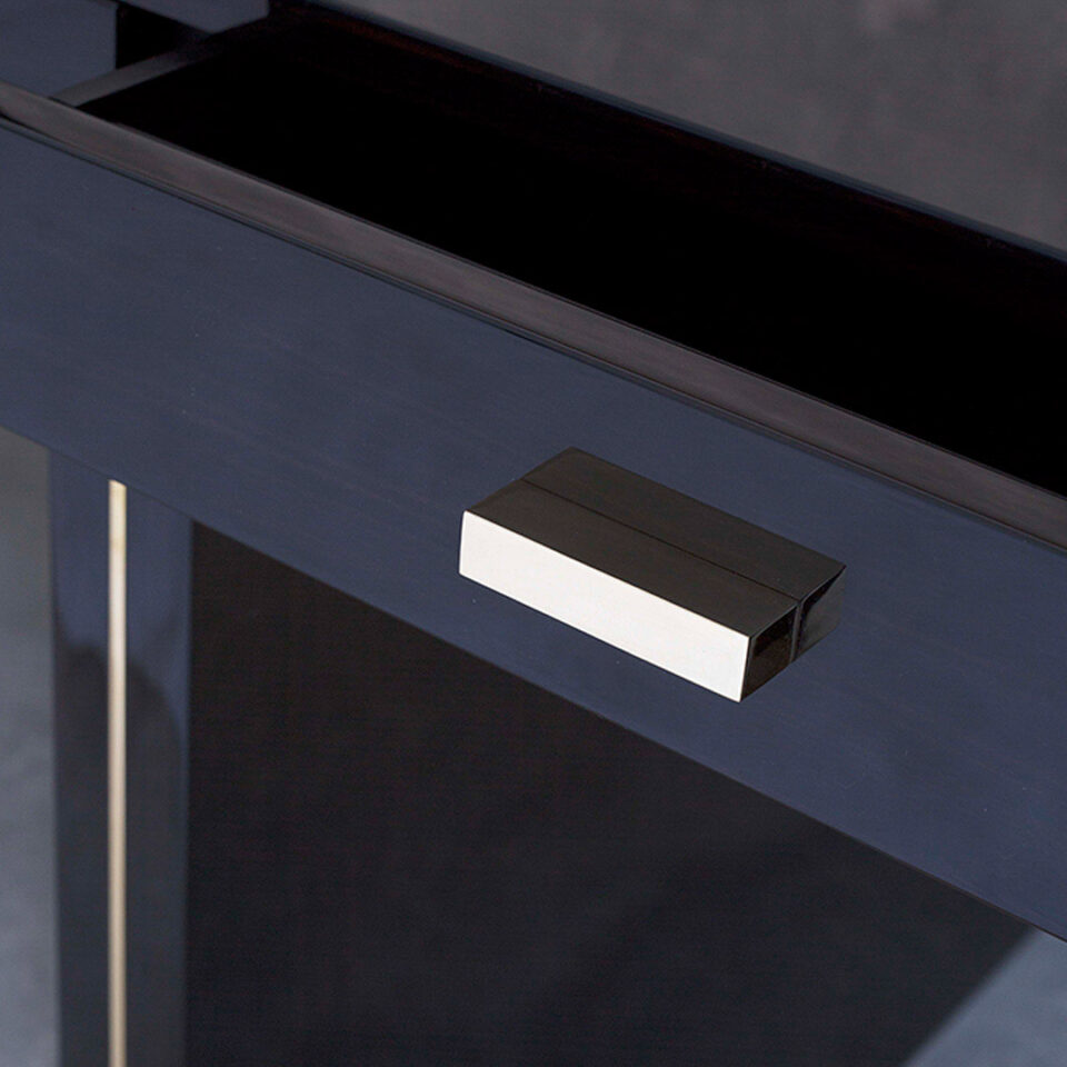 A sleek sophisticated desk with a long slender table top supported by two legs. Finished in a high gloss sycamore black with luxurious brushed brass highlights