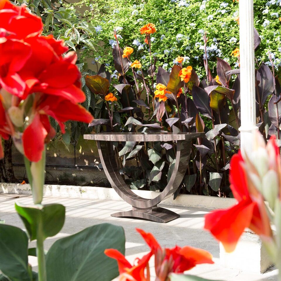 A sleek console table with a wide, curve base finished in a high gloss figured eucalyptus tinted in a smart shade of grey with a polished nickel inlay detail to the base. Design by DAVIDSON London