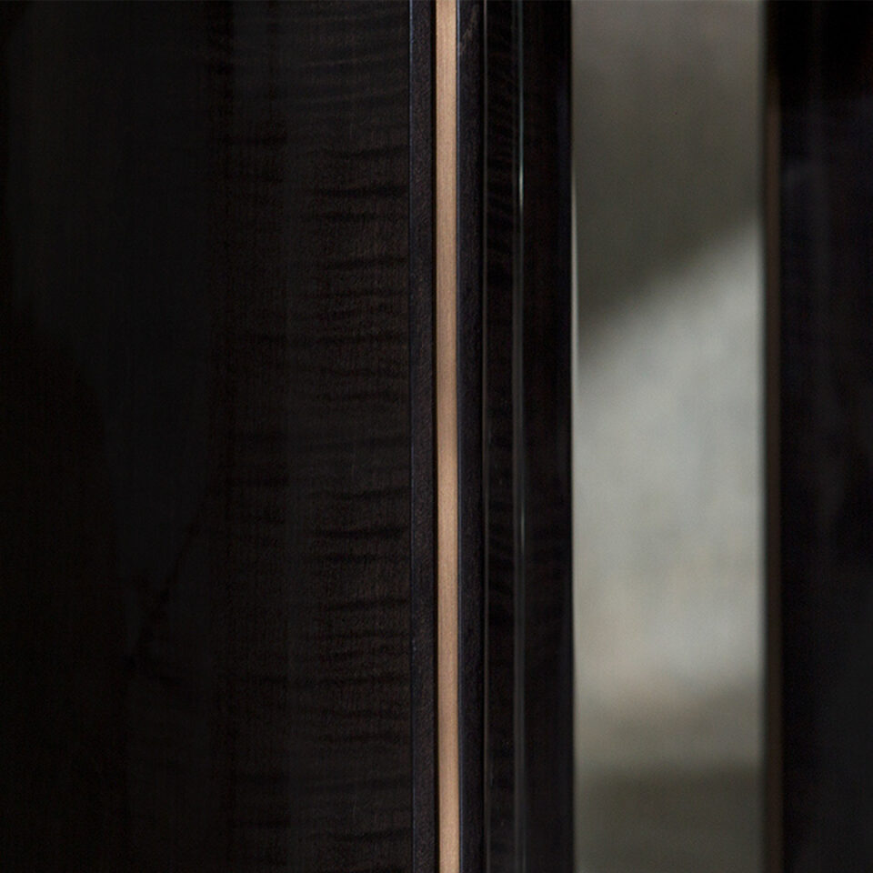 A detail image of this contemporary dining table’s pedestal finished in a high gloss sycamore black with a glamorous antiqued brushed brass trim.
