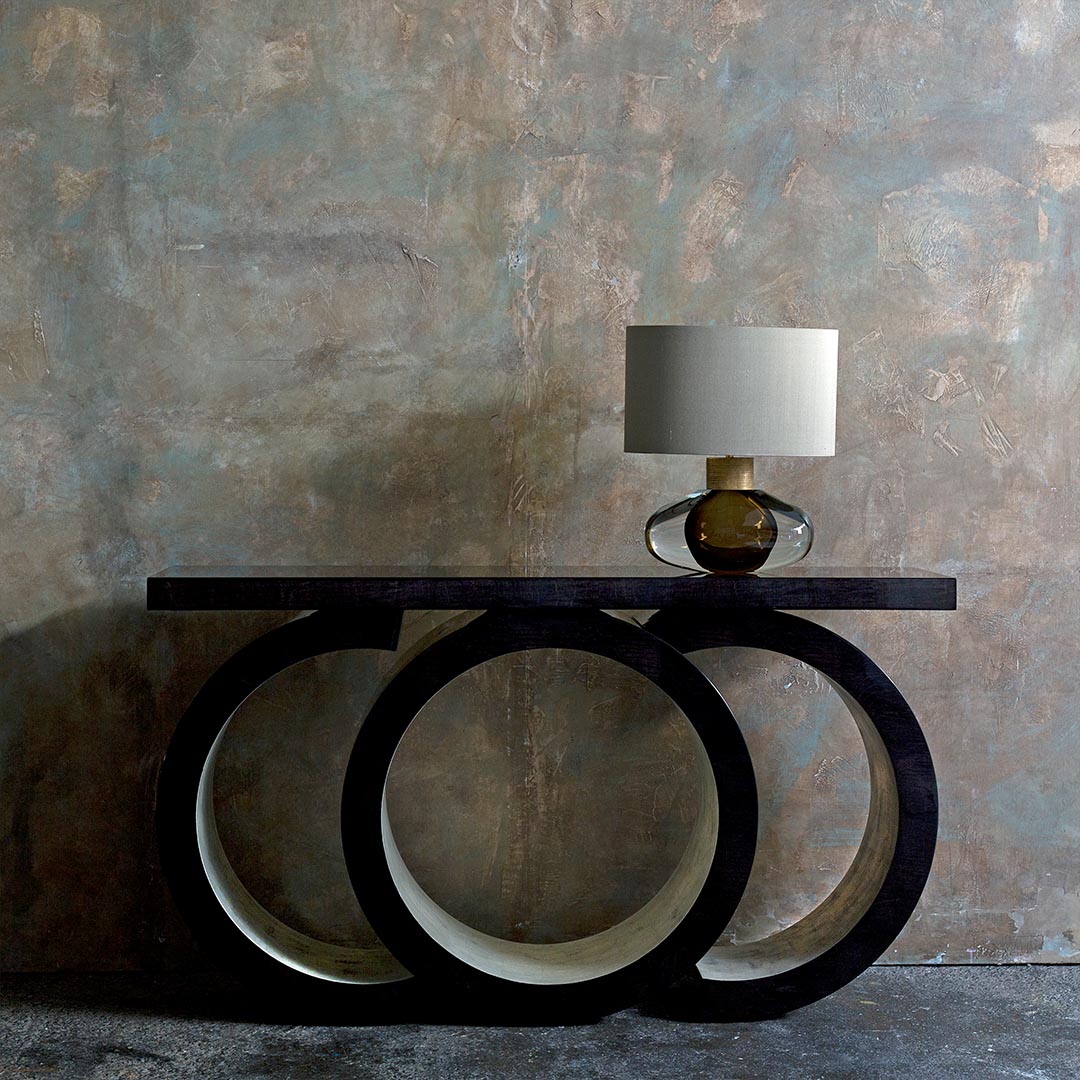 A contemporary console with an eye-catching sculptural silhouette finished in a high gloss sycamore black with distressed white gold leaf detailing.
